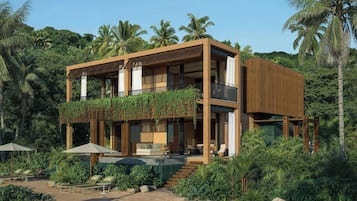 Un edificio moderno de dos pisos con balcón, asientos al aire libre y abundante vegetación.