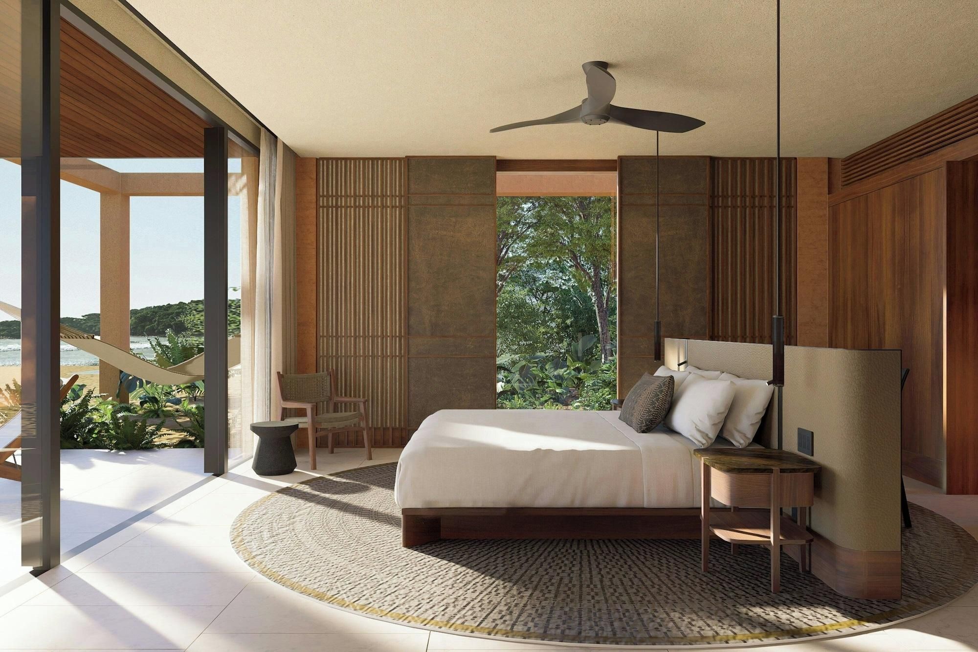 A bedroom with a bed, a ceiling fan, a nightstand, a chair, and a view of the outdoors.