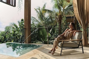 Una persona sentada en una silla junto a una piscina, con vistas a plantas tropicales y un cielo despejado.
