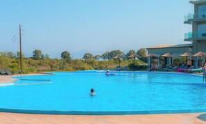 A swimming pool with lounge chairs and umbrellas, surrounded by greenery and a building. - Laguna Holiday Resort Corfu (Corfu)