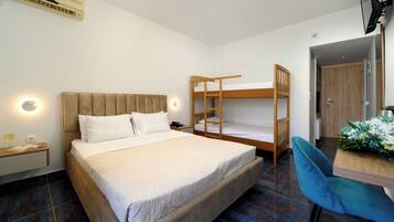 Un dormitorio con una cama grande, una cama litera, un escritorio con silla y una mesita de noche con lámpara.