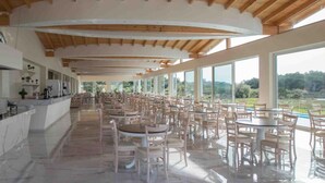 A spacious indoor area with a high ceiling and large windows, featuring multiple tables and chairs arranged for dining. - Laguna Holiday Resort Corfu (Corfu)