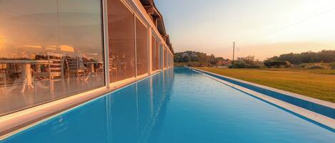 A swimming pool with a glass enclosure, a view of the landscape, and a clear sky.