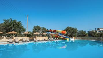 Una piscina con tobogán de agua, sillas de descanso y sombrillas.