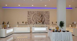 A modern hotel lobby with three reception counters, a central decorative wall, and a round table with amenities. - Laguna Holiday Resort Corfu (Corfu)