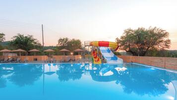 Una piscina con tobogán, sillas de descanso y sombrillas.