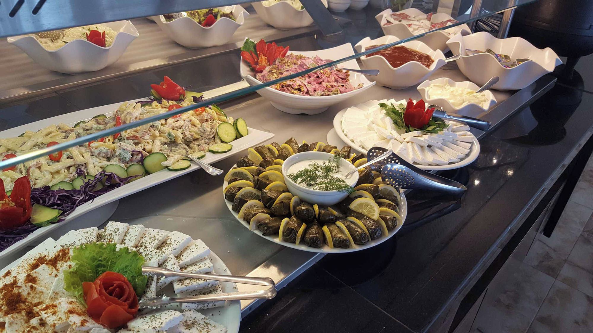 Ein reichhaltiges Buffet mit verschiedenen Gerichten, darunter Pasta-Salat, gefüllte Weinblätter und Käseplatten.