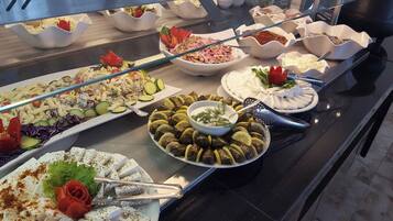 Ein reichhaltiges Buffet mit verschiedenen Gerichten, darunter Pasta-Salat, gefüllte Weinblätter und Käseplatten.