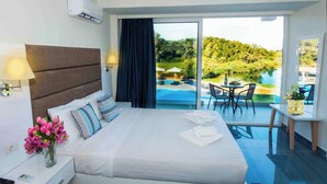 A hotel room with a bed, a nightstand, a lamp, a vase of flowers, a view of a pool and outdoor seating. - Laguna Holiday Resort Corfu (Corfu)