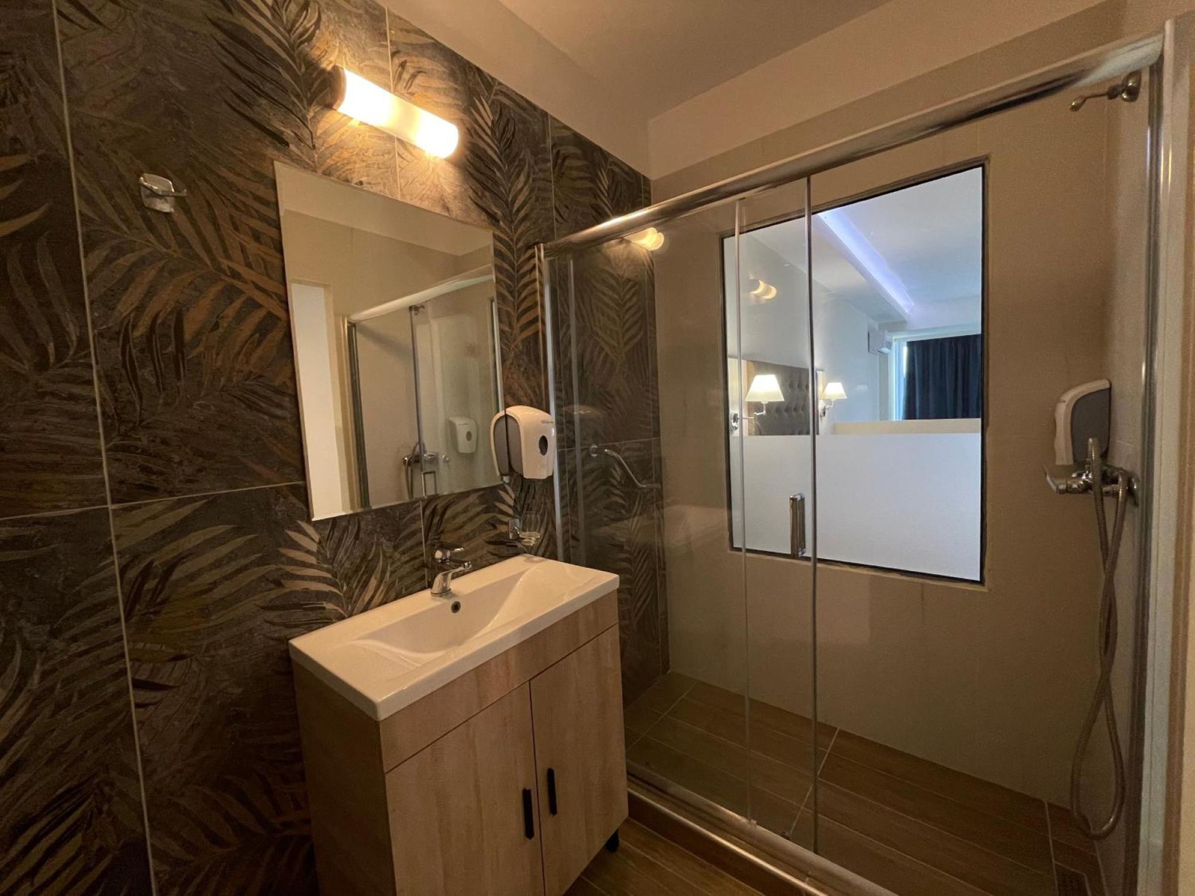 Ein modernes Badezimmer mit Duschkabine aus Glas, Waschbecken mit Spiegel und Handseifen-Spender.