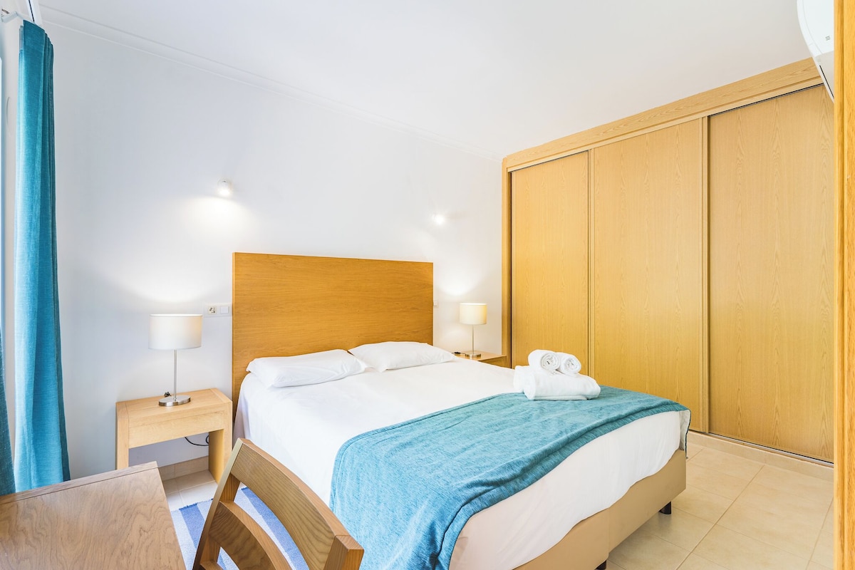 A hotel room with a bed, bedside tables, a desk, and a wardrobe.