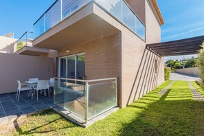 A modern house with a glass balcony, a patio with chairs, and a well-maintained lawn. - Lumina Villas (Lagoa)