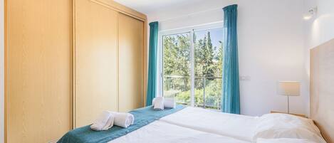 Ein Hotelzimmer mit einem großen Bett, einem Holzschrank, einem Fenster mit Vorhängen und einem Nachttisch mit Lampe.