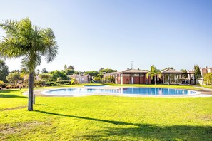 A swimming pool surrounded by a well-maintained lawn, a palm tree, and a building with a tiled roof. - Lumina Villas (Lagoa)