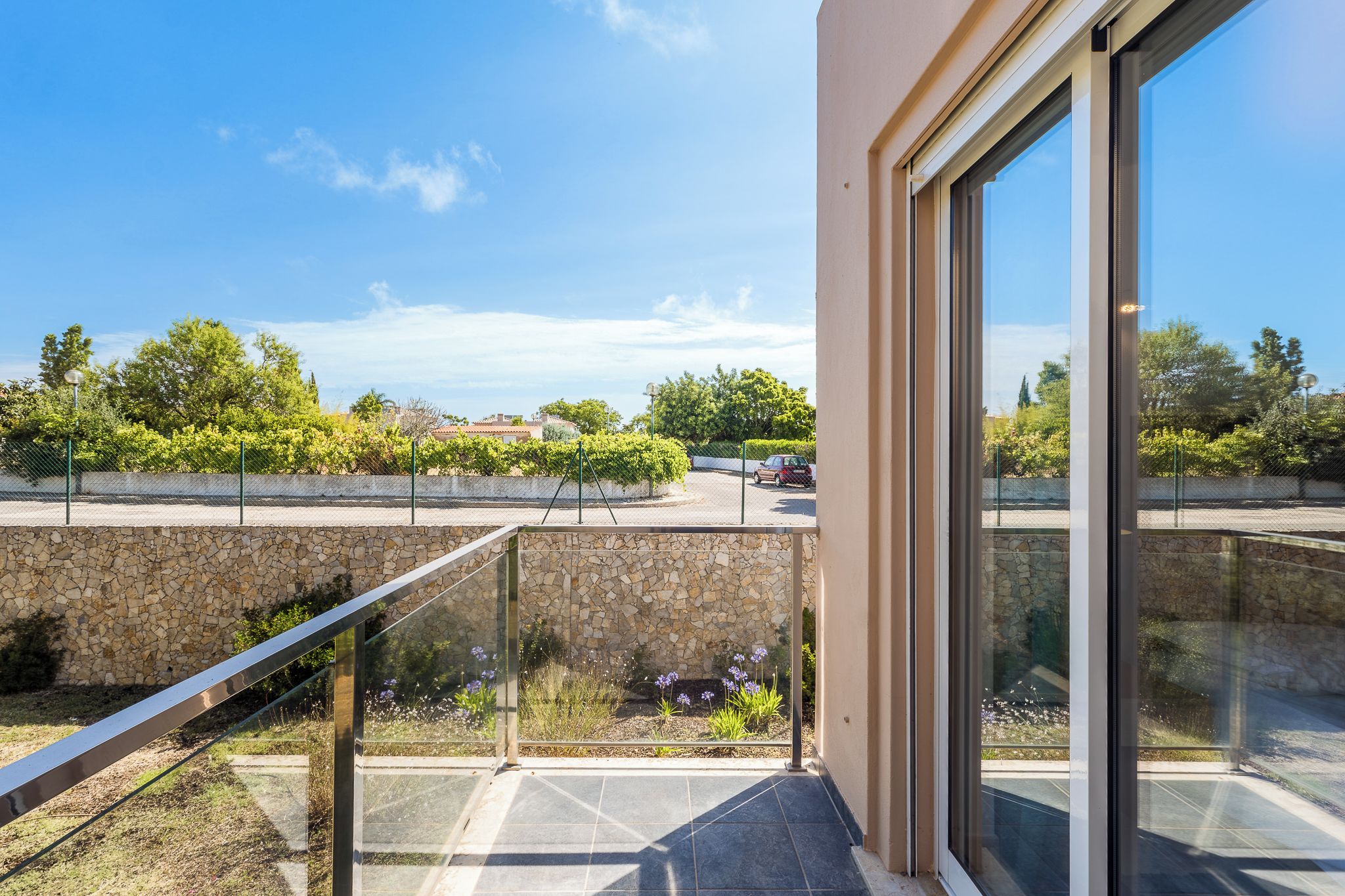 A balcony with a stone wall, a glass railing, and a view of a residential area.