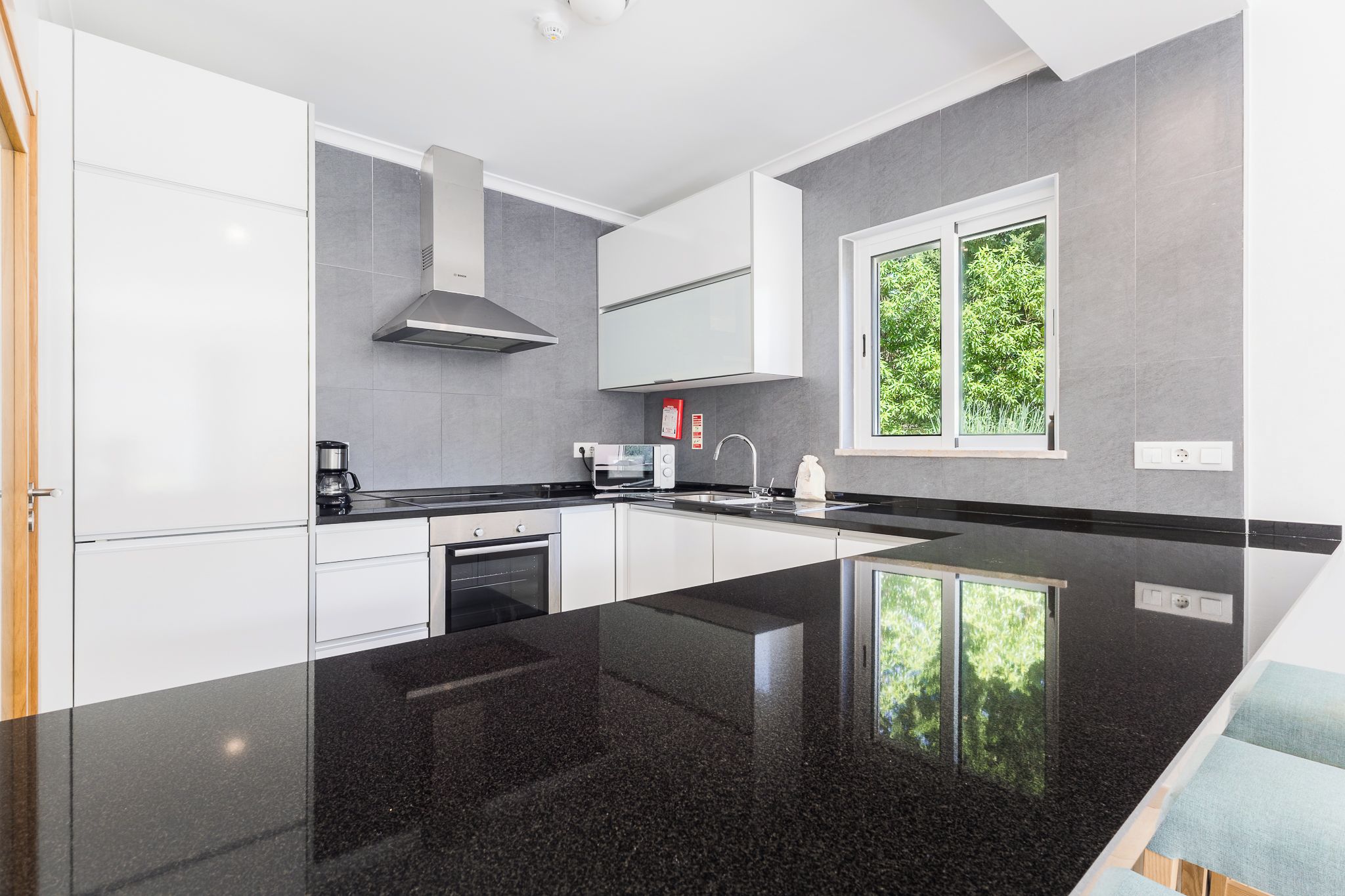 Cocina moderna con armarios blancos, encimera negra y ventana con vistas a la vegetación.