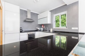 A modern kitchen with white cabinets, a black countertop, and a window with a view of greenery. - Lumina Villas (Lagoa)