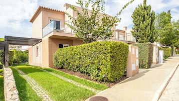 Una casa moderna de dos pisos con balcón, césped cuidado y un muro de piedra.