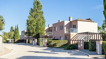 A modern residential building with a paved driveway, a covered outdoor area, and a well-maintained garden.