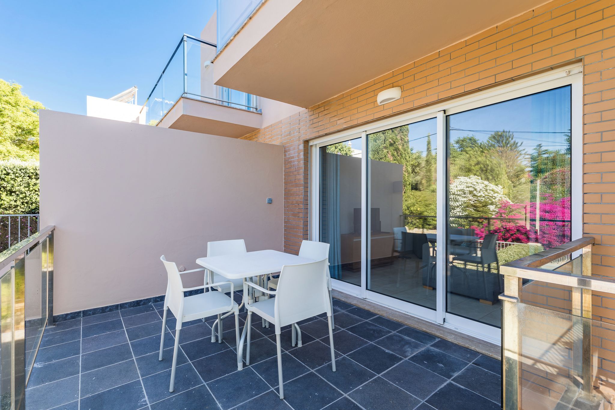 A balcony with a glass door, white chairs, and a table.