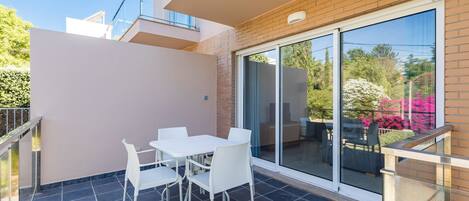 A balcony with a glass door, white chairs, and a table.
