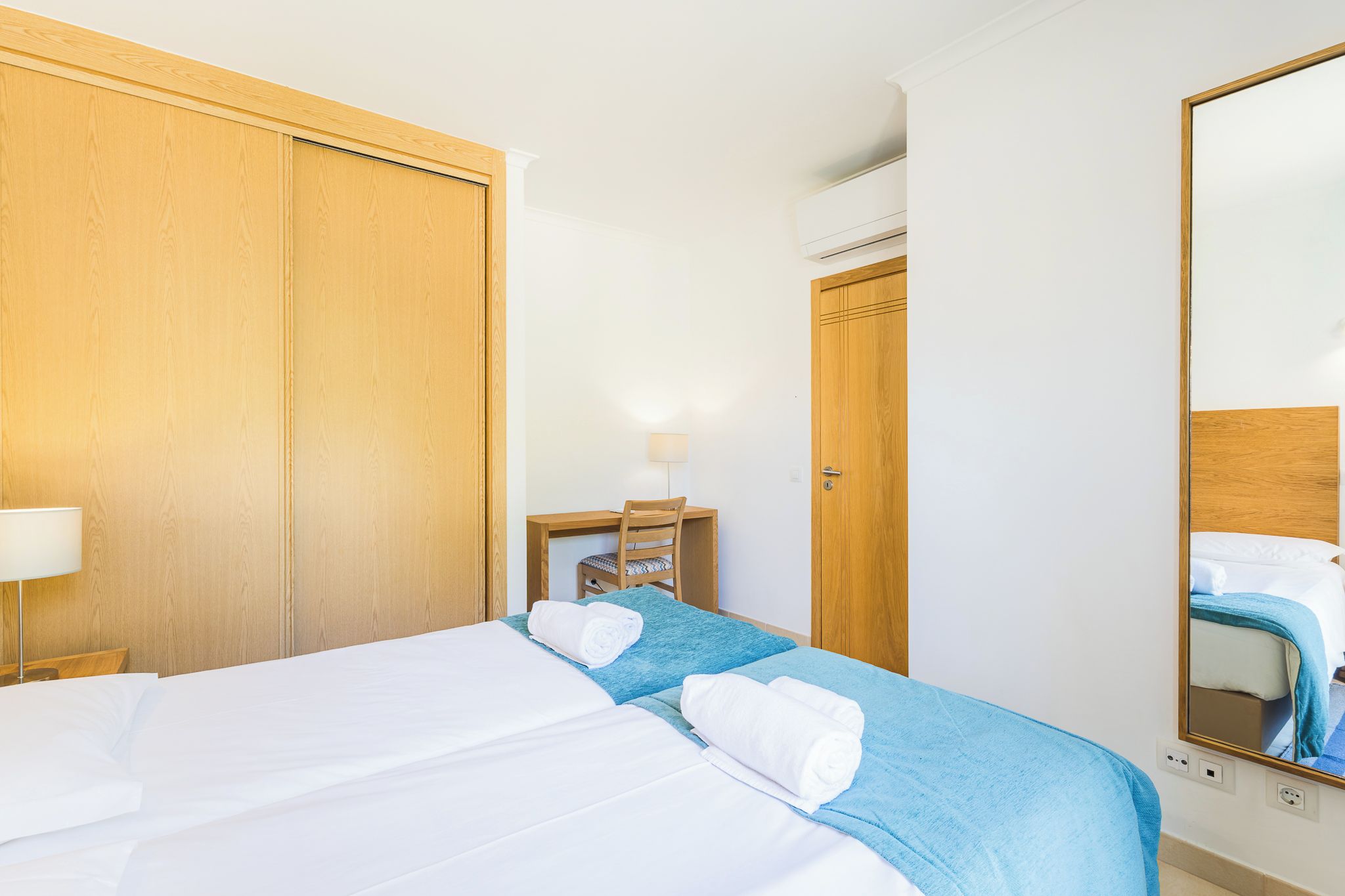 A hotel room with a bed, a desk, a chair, a mirror, and a wardrobe.