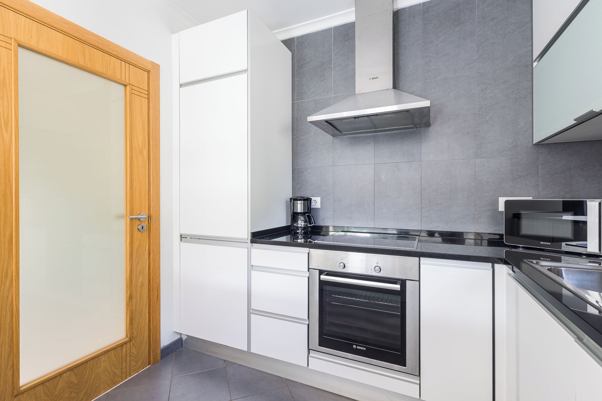 A modern kitchen with white cabinets, a Bosch oven, a microwave, and a coffee maker.