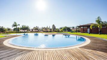 A swimming pool with a wooden deck, surrounded by greenery and buildings.