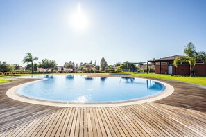 A swimming pool with a wooden deck, surrounded by greenery and buildings. - Lumina Villas (Lagoa)