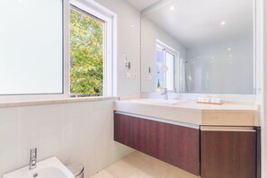 A modern bathroom with a large mirror, a sink, and a window with a view of greenery. - Lumina Villas (Lagoa)