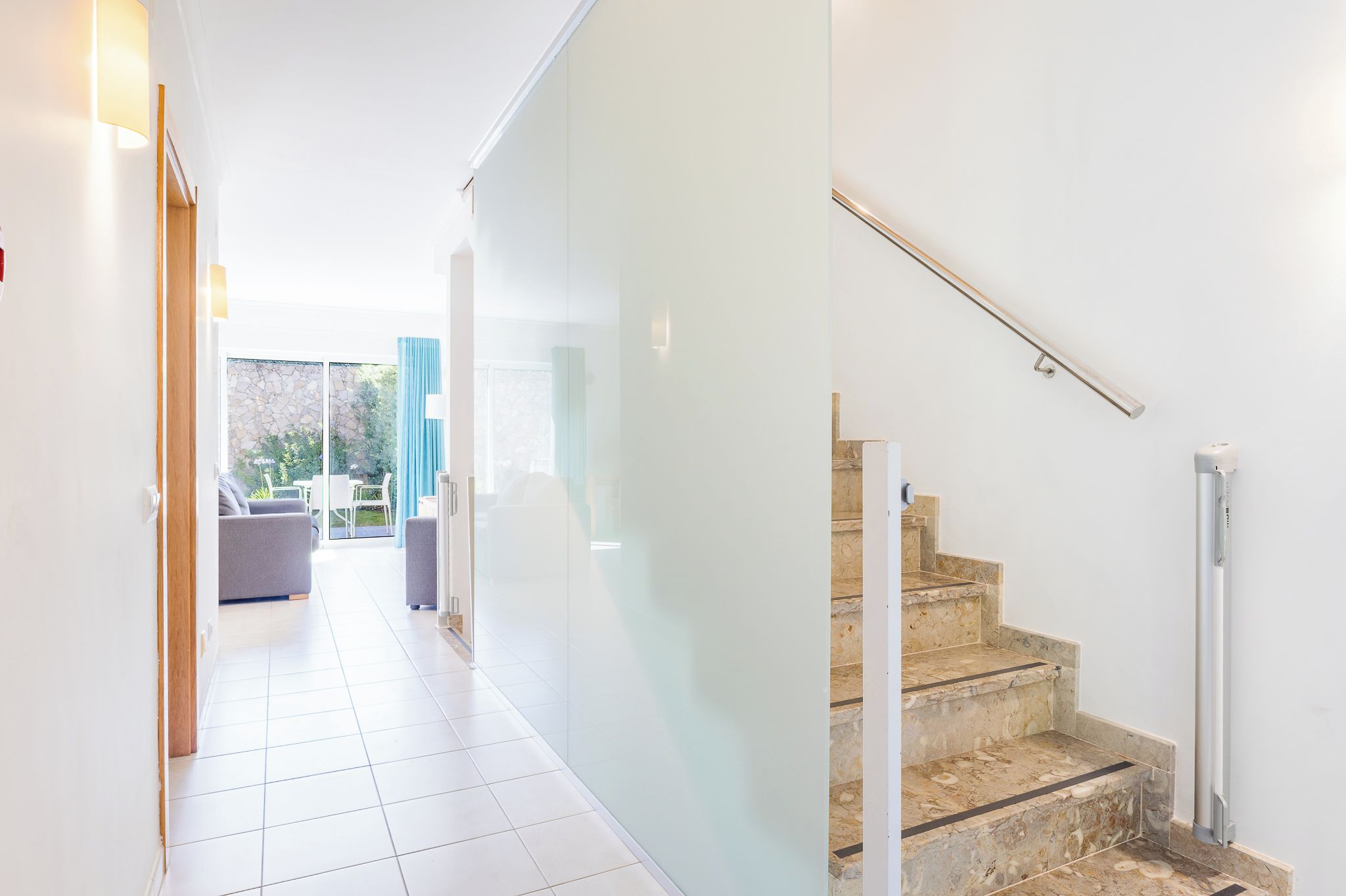 Un interior moderno con una escalera, un pasillo que conduce a una zona de estar y un ventanal hacia el exterior.