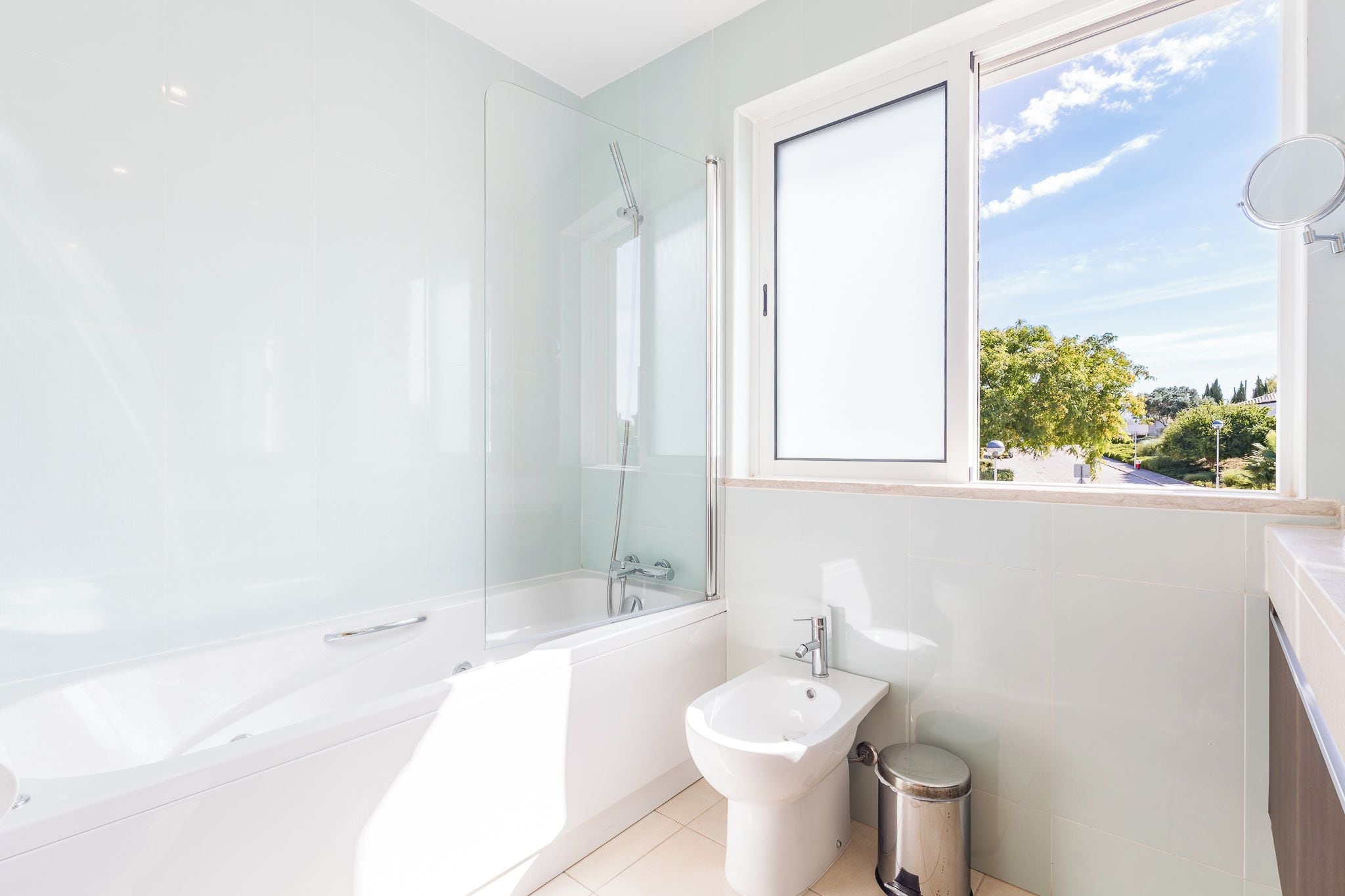 Un baño moderno con ducha envuelta en vidrio, una bañera independiente, un bidé y un ventanal con vistas al exterior.