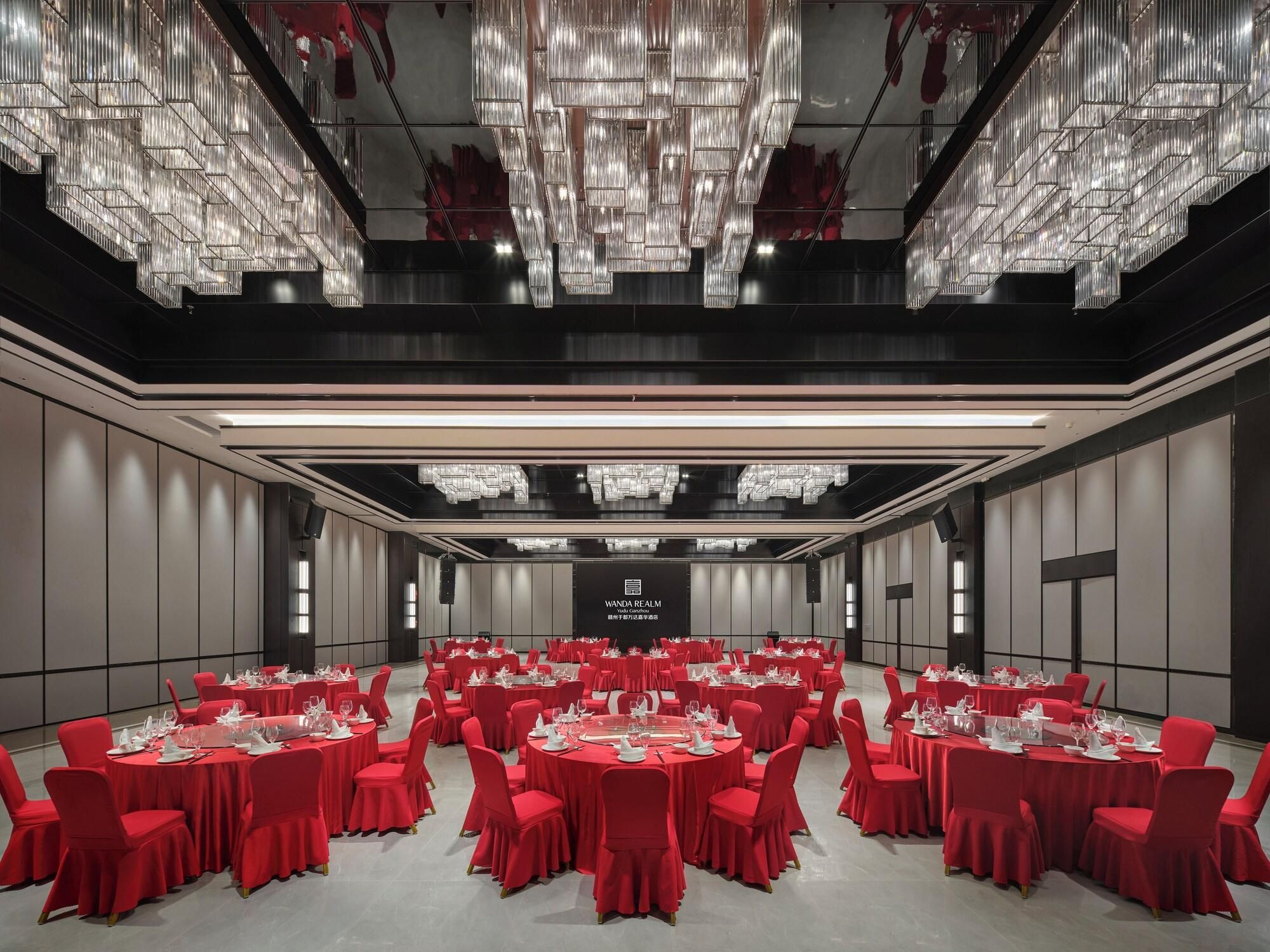 Une salle de conférence avec des tables rondes, des chaises rouges et un lustre.