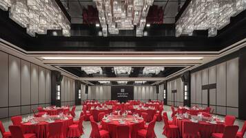 Une salle de conférence avec des tables rondes, des chaises rouges et un lustre.
