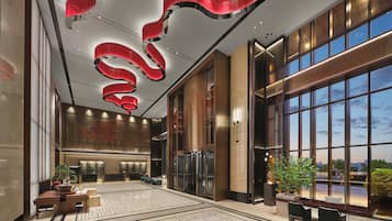 A spacious lobby with a modern design, featuring a large reception desk, seating area, and large windows offering a view of the cityscape.