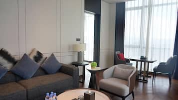 A modern hotel room with a sofa, armchair, small round table, and a dining area with chairs.
