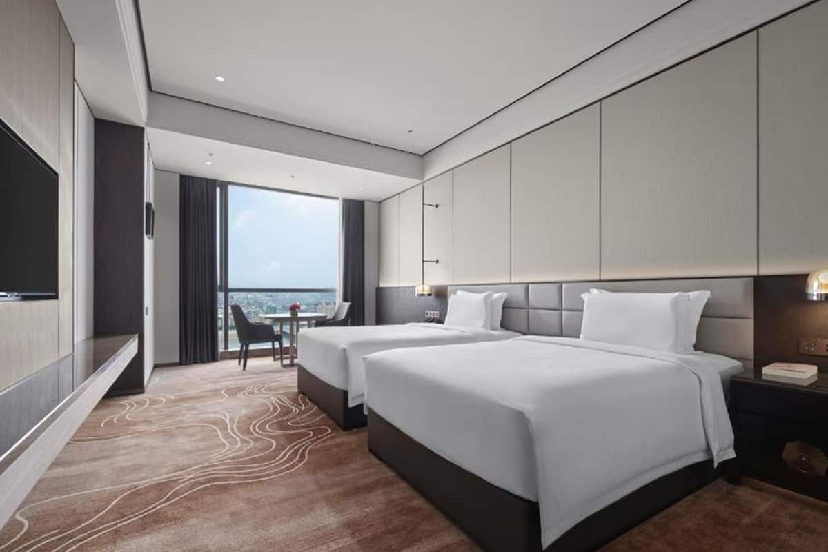 A hotel room with two beds, a TV, a desk with a chair, and a view of the city.