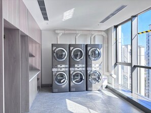 Un moderno lavadero con cuatro lavadoras apiladas, ventanas amplias y vista a la ciudad.