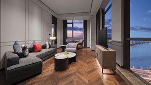 A modern hotel room with a large sofa, a coffee table, a TV, and a view of a cityscape and water. - Wanda Realm Yudu Ganzhou (Guangzhou)