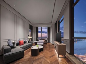 Una habitación de hotel moderna con un sofá grande, una mesa de centro, un televisor y vistas a la ciudad y al agua.