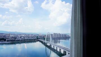 A cityscape with a bridge over a calm body of water, distant mountains, and a clear sky.