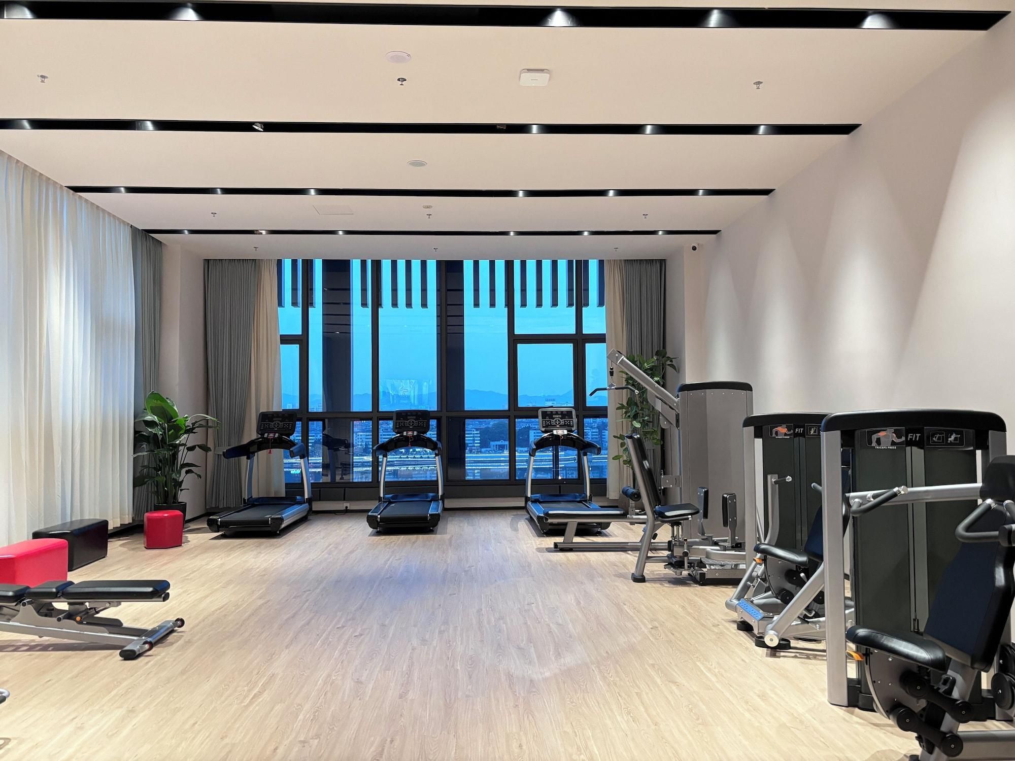 A modern gym with treadmills, weight machines, and a large window with a city view.