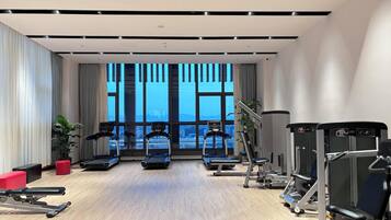 A modern gym with treadmills, weight machines, and a large window with a city view.
