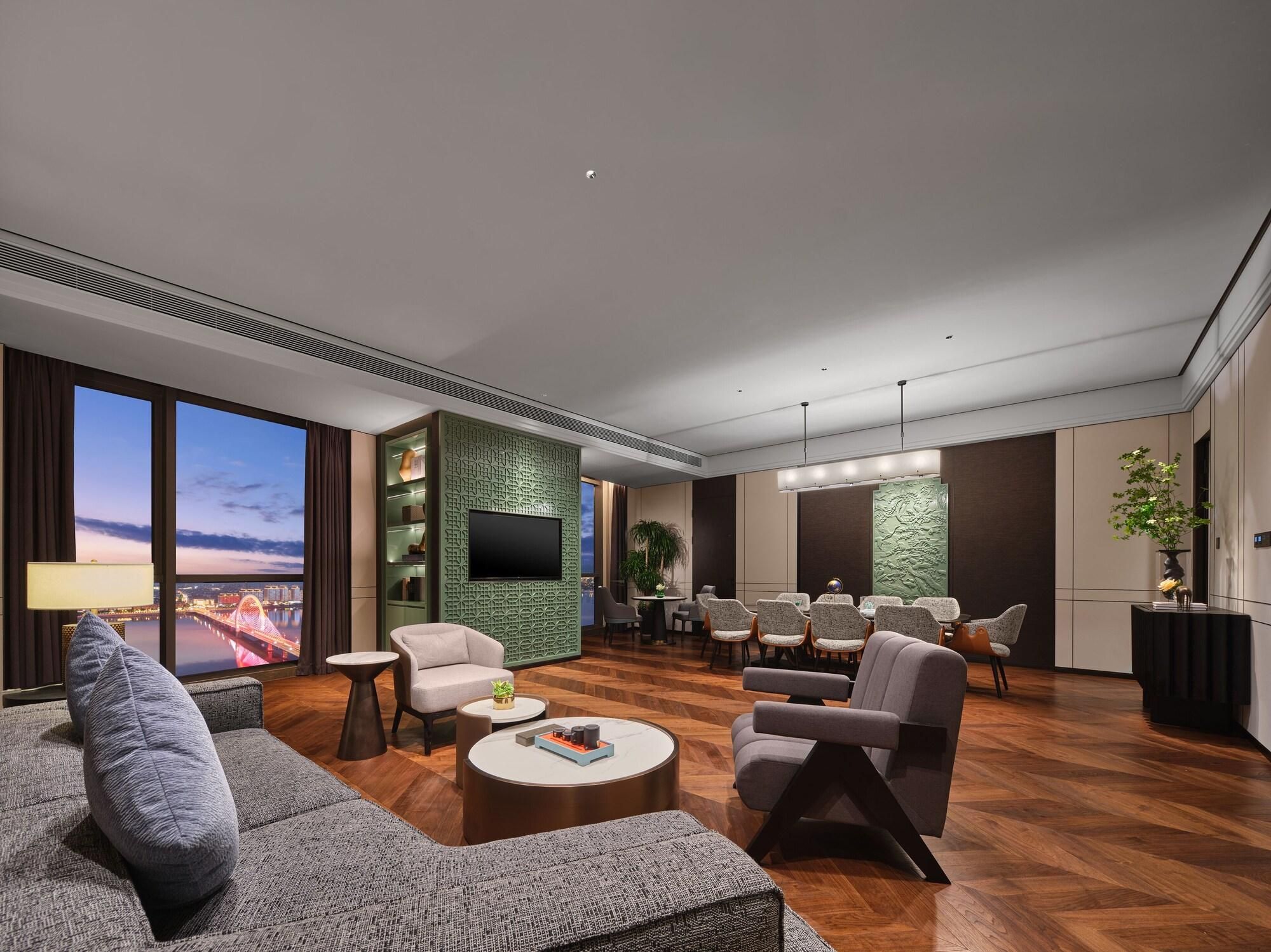 A modern living room with a large TV, comfortable seating, a dining area, and a view of a cityscape.