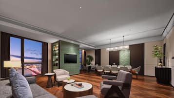 A modern living room with a large TV, comfortable seating, a dining area, and a view of a cityscape.