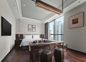 Una habitación de hotel moderna con una cama grande, un escritorio con taburetes, un televisor de pantalla plana y un amplio ventanal con vistas a la ciudad.