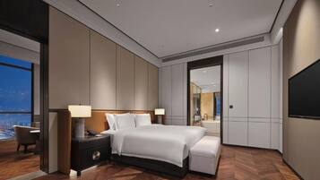 A modern hotel room with a large bed, bedside tables, a desk, a chair, and a large window offering a city view.