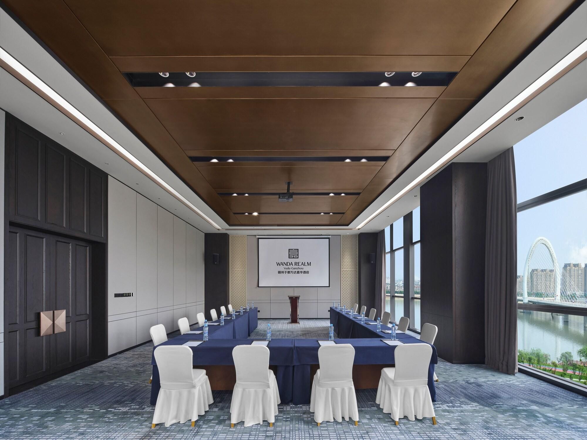 A conference room with a long table, chairs, a projector screen, and a view of a cityscape.