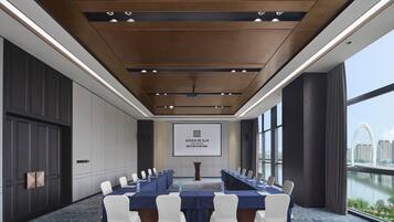 A conference room with a long table, chairs, a projector screen, and a view of a cityscape.