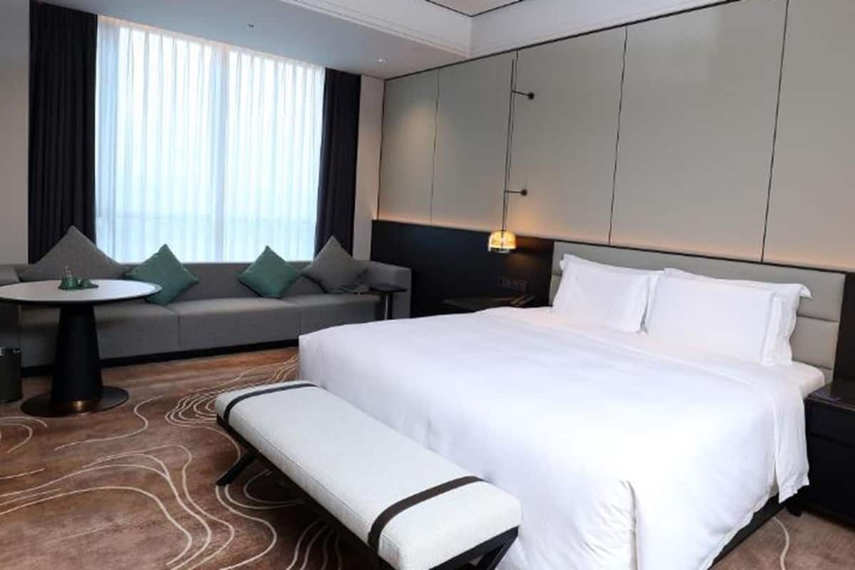 A hotel room with a bed, a bench, a sofa, a small table, and a lamp.